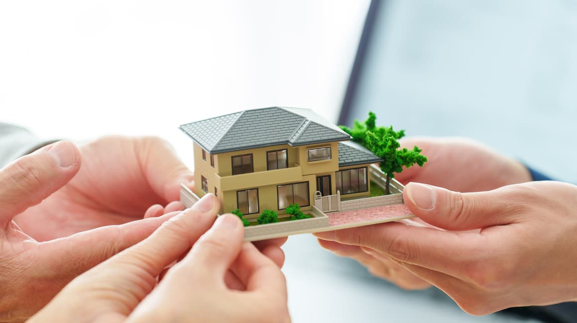  Due mani di persone diverse si incontrano per reggere insieme un piccolo modello di casa, simboleggiando il passaggio di proprietà immobiliare e i processi di successione. Scopri le differenze chiave tra successione legittima e testamentaria e le implicazioni pratiche per i tuoi diritti e i tuoi doveri.